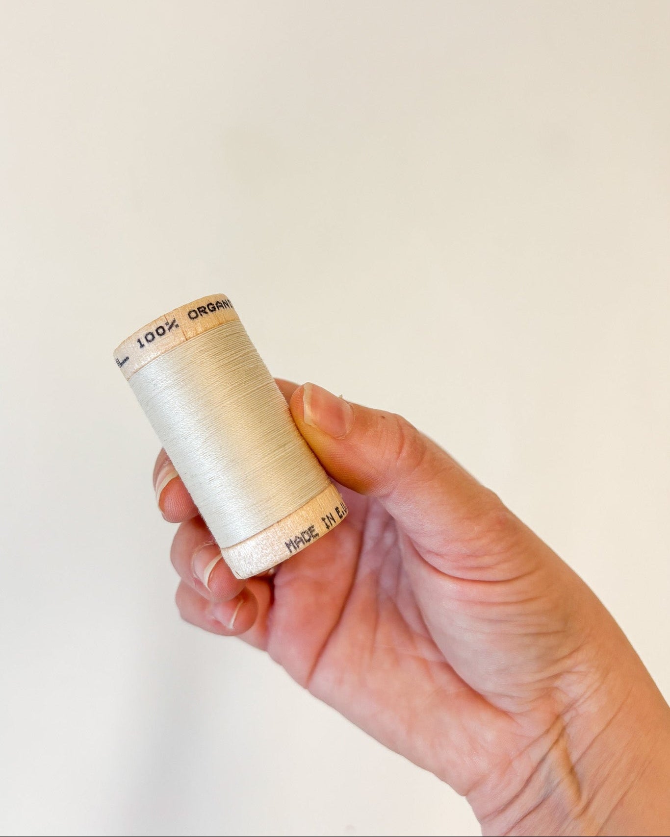 Hand holding a spool of thread against a plain background organic cotton thread