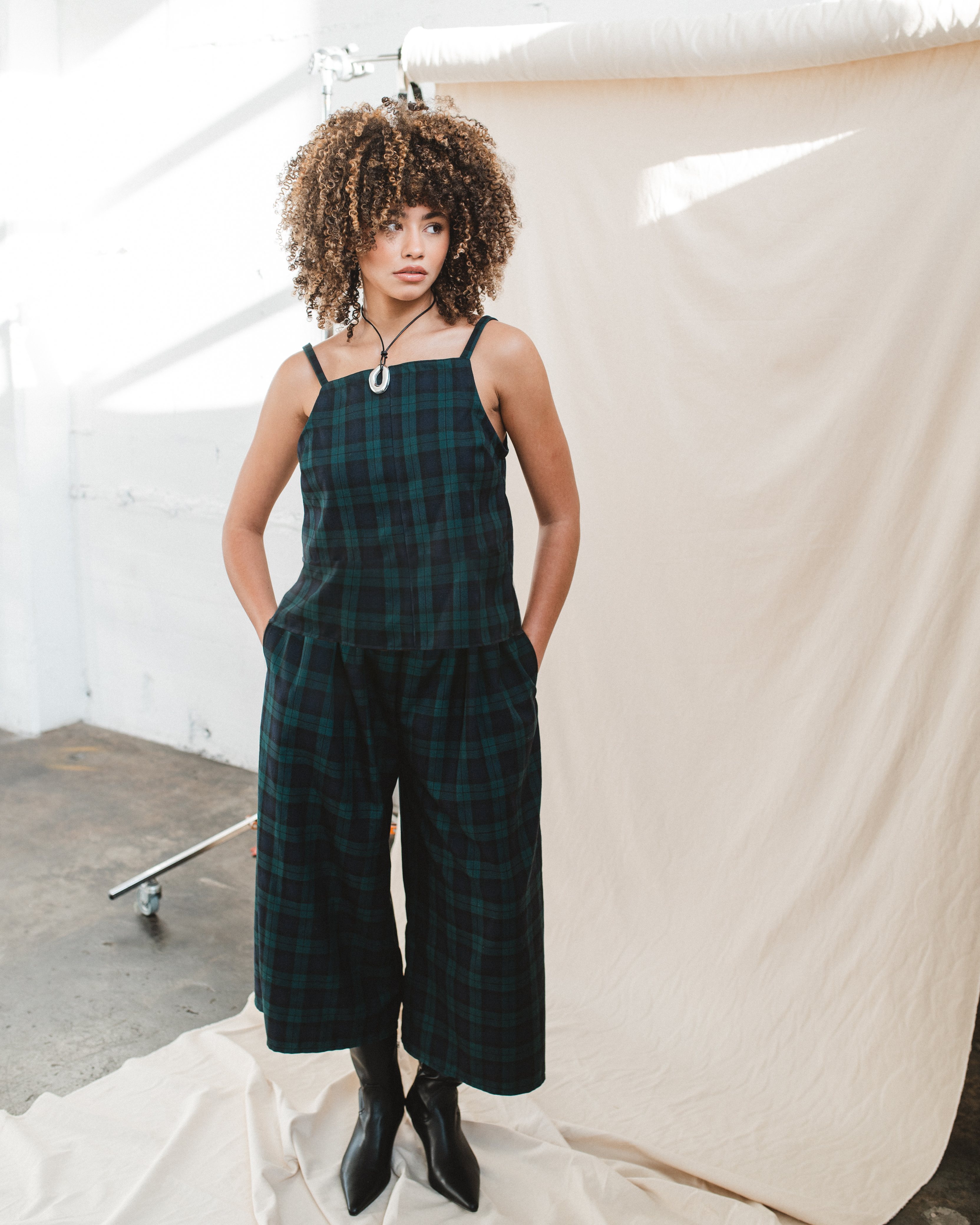 Person wearing a green plaid dress with black boots in an indoor setting.