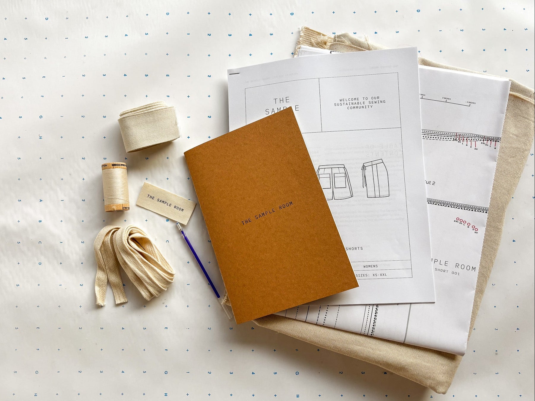 Brown notebook, spool of thread, and fabric samples on a white surface with a polka dot pattern.